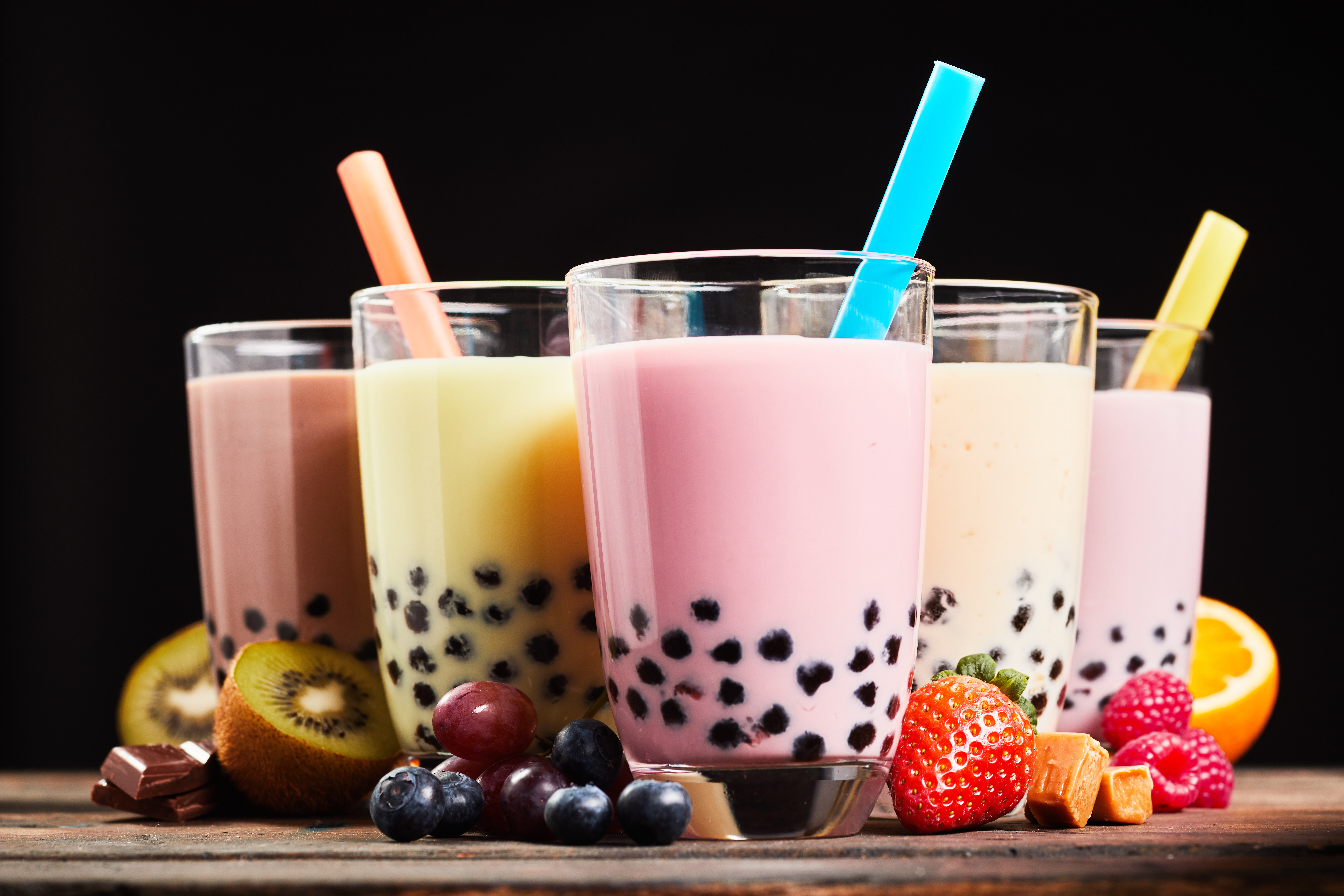 Glasses of refreshing milky boba or bubble tea with assorted fresh fruit ingredients, chocolate and caramel candy used as flavoring, low angle side view